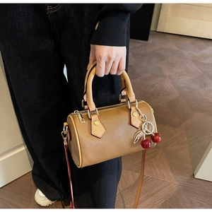 Detail of mini Boston bag in brown pebble leather with red edges and cherry charm