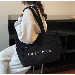 Détail du sac cabas en velours côtelé noir avec broderie porté par un mannequin