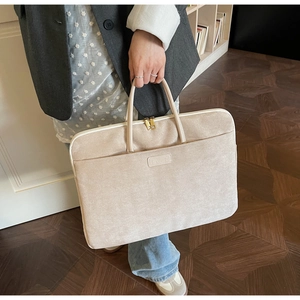 Elegant beige suede laptop bag with leather handles and gold zipper shown in use