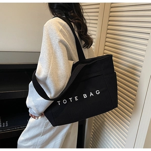 Détail d'un grand sac cabas en velours côtelé noir porté à l'épaule par un mannequin