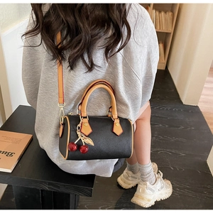 Detail of black pebbled leather Boston bag with tan handles and cherry charm on side
