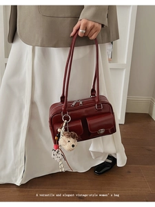 Detailed close-up of a vintage wine red shoulder bag with two pockets and a cute puppy charm