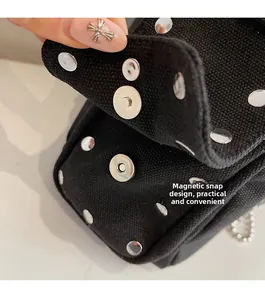 Detail of silver rivets and magnetic snap closure on a black canvas crossbody bag