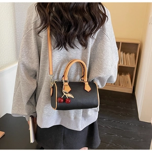 Detail of a black mini Boston bag with cherry charm and leather strap on a model