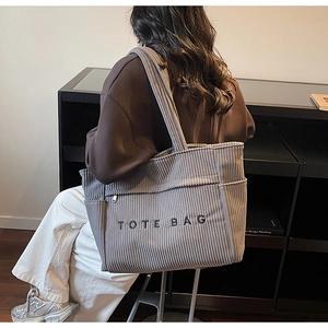 Détail d'un grand sac fourre-tout en velours côtelé gris avec broderie porté par un modèle