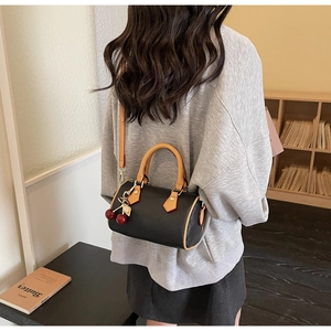 Boston style crossbody bag with black leather and cherry charm shown in a lifestyle scene