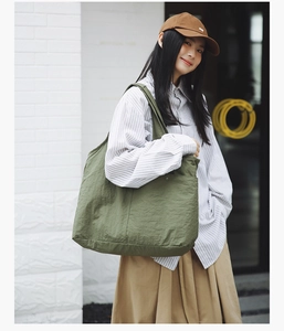 Détail d'un grand sac fourre-tout en nylon vert porté avec une chemise à rayures