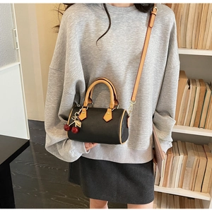 Detail of black pebbled leather Boston bag with cherry charm shown on shoulder