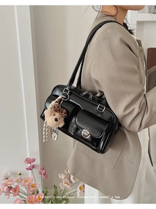 Detail of glossy black shoulder bag with multi-pockets and cute teddy bear charm