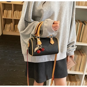 Detail of black Boston bag with contrasting yellow handles and cherry charm in a library
