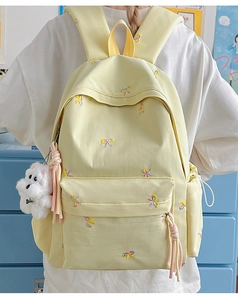 Detail of light yellow backpack with bow embroidery and cute plush dog pendant charm