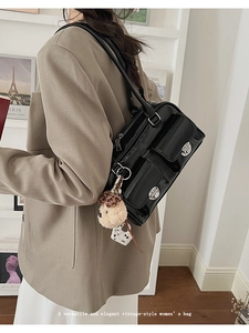 Close-up of black patent leather shoulder bag with silver buckles and plush charm