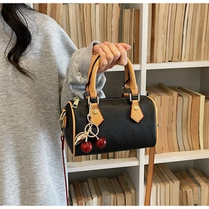Detail of Boston-style barrel bag with cherry pendant and brown handles in a lifestyle setting