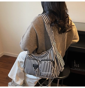 Detail of striped tote bag featuring metallic studs, chain accents, and zipper pockets
