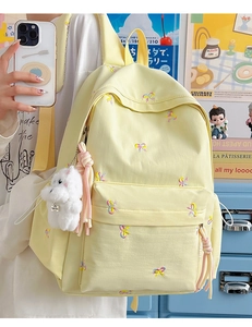 Detail of yellow school backpack with colorful bow embroidery and white plush puppy charm