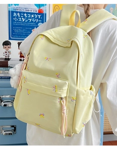 Detail of yellow school backpack with colorful bow embroidery and white plush pendant