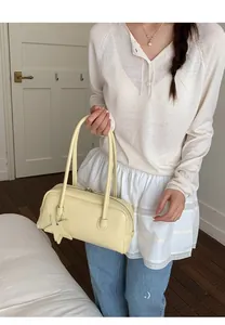 Détail d'un sac baguette en cuir jaune clair avec charm étoile porté à l'épaule