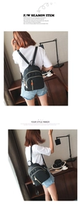 Detail of a black nylon backpack with gold zippers shown on a model in a home setting
