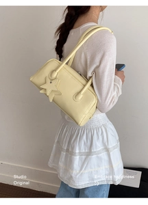 Détail d'un sac à bandoulière jaune crème avec breloque étoile et fermeture éclair sur tenue