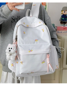 Detailed view of white backpack with colorful bow embroidery and plush puppy pendant accessory