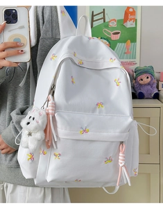 Detailed close-up of white backpack with colorful bow embroidery and plush puppy pendant