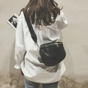 Detail of a black half-moon waist bag with silver zipper and wide textile strap on model