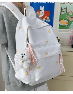 Detail of white canvas backpack featuring colorful bow prints and a cute plush dog pendant