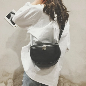 Close-up of a crescent-shaped black leather fanny pack with silver zippers on a model