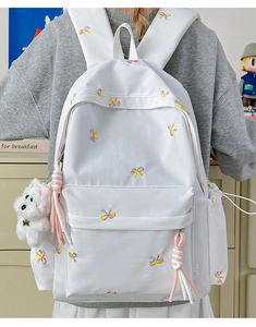 Detail of white leather backpack with colorful bow embroidery and cute plush dog pendant