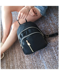 Mini black nylon backpack with golden zippers shown in a lifestyle handheld use pose