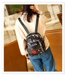 Detail of black sequin backpack with LOVE embroidery and red lip patch on a model
