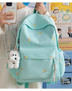 Detail view of mint green nylon backpack with colorful bow embroidery and fuzzy dog charm