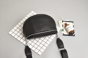 Detail view of black semi-circular crossbody bag with silver zipper on a white grid