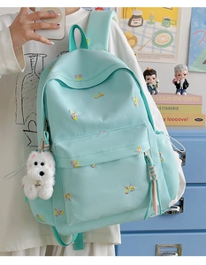 Detail of mint green nylon backpack featuring colorful bow embroidery and a plush puppy charm