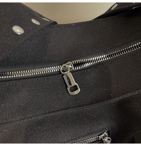 Close-up of black canvas bag featuring silver metal zipper and round stud details