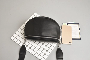Detail of a black crescent crossbody bag with silver zipper and wide shoulder strap