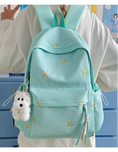 Detail of mint green backpack featuring colorful bow embroidery and plush dog charm
