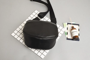 Detail of black semi-circular leather waist bag with silver zipper and nylon strap