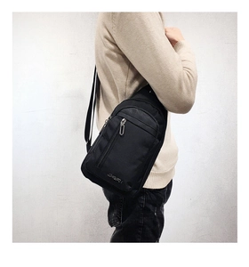 Detail of black crossbody chest bag with vertical zipper and metal hardware on model
