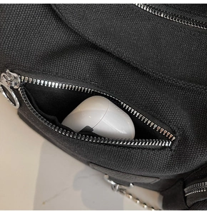 Close-up of front zipper pocket on black canvas bag showing storage capacity for earbuds