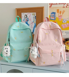 Detail of mint green and light pink backpacks with embroidered bows and plush puppy charms