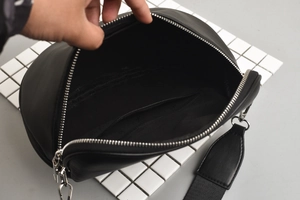 Detail view of black waist bag showing internal compartment with silver zipper and wide strap