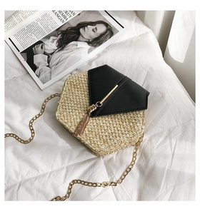 Detail of hexagonal straw crossbody bag with black leather flap and gold tassel fringe