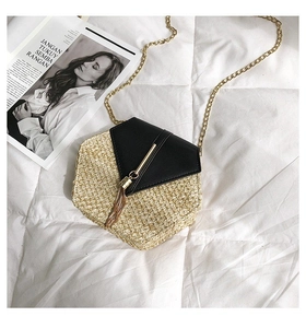 Detail of hexagonal straw crossbody bag with black leather flap and gold tassel decor