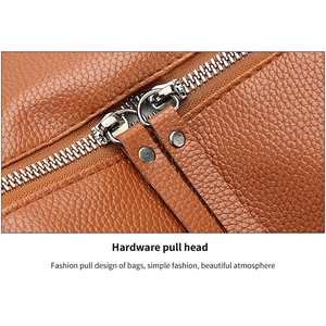 Detail view of the silver dual metal zippers and lychee grain leather on the brown backpack