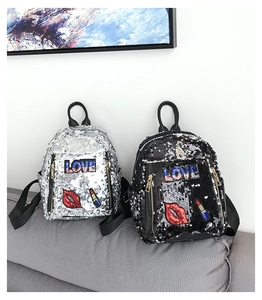 Detail of silver and black sequin mini backpacks featuring Love and lip embroidery on sofa