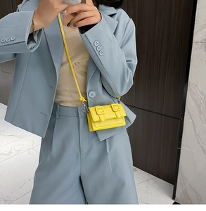 Detail of yellow mini crossbody bag in textured faux leather with double buckle flap