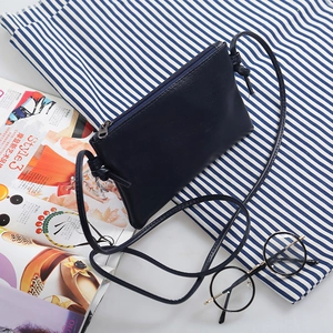 Minimalist navy blue mini crossbody bag with zipper and slim strap on lifestyle background