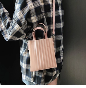 Détail d'un sac à bandoulière plissé rose porté par un mannequin en chemise