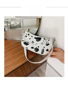 Detail view of cow print baguette bag with transparent acrylic chain and zipper on wood surface